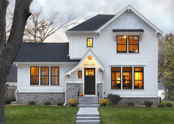 Macfarlane windows and doors story of the home Charming white house with black-framed windows and doors by Macfarlane Windows and Doors, featuring warm interior lighting and a welcoming front entrance.