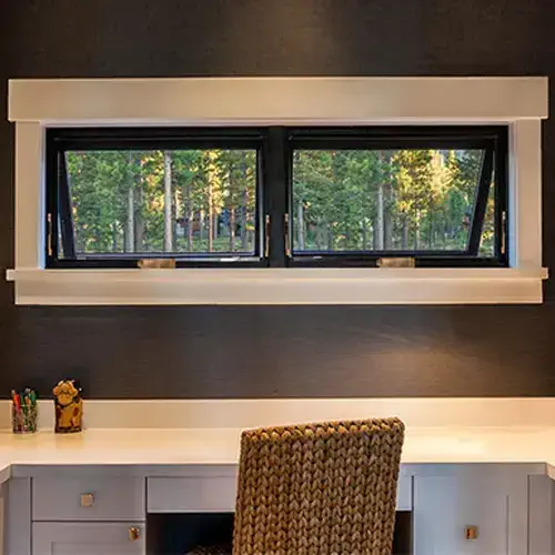 awning window 2 macfarlane Awning windows above a table, showcasing their ability to be open and keep out the rain. Modern and stylish, black frames with grey walls, backlit in a home.