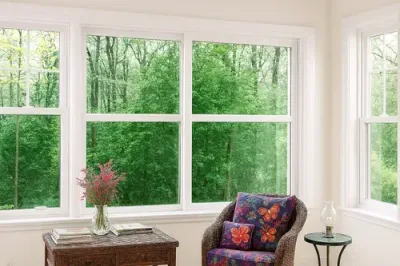 new living room sliders (1) Cozy sunlit living space with multiple white-framed slider windows installed by MacFarlane Windows and Doors, offering a clear view of the lush green outdoors.